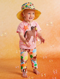 Child wearing a colorful hat and animal-themed shirt and leggings on a yellow background with bubbles.