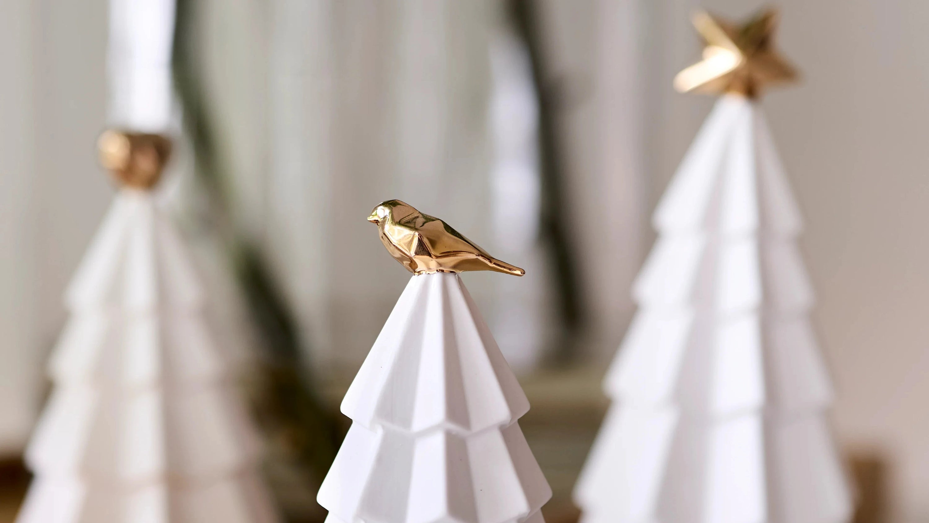 White geometric Christmas trees with gold birds on a marble surface