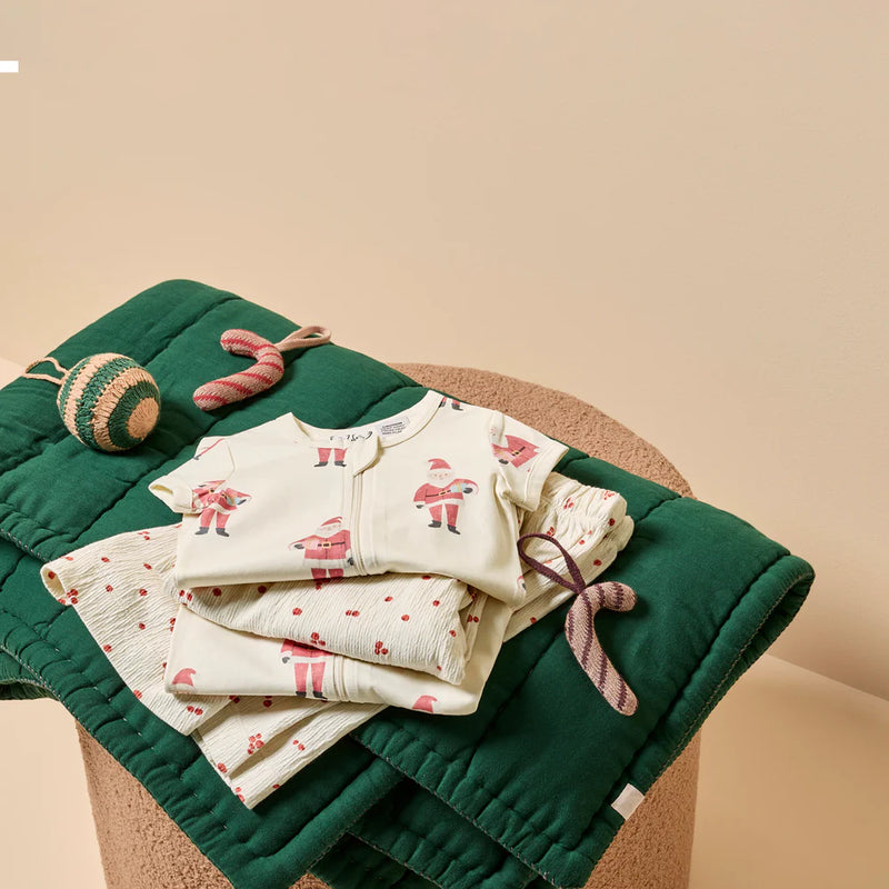 Baby outfit with beige and red Christmas Santa on a green blanket and christmas decorations.