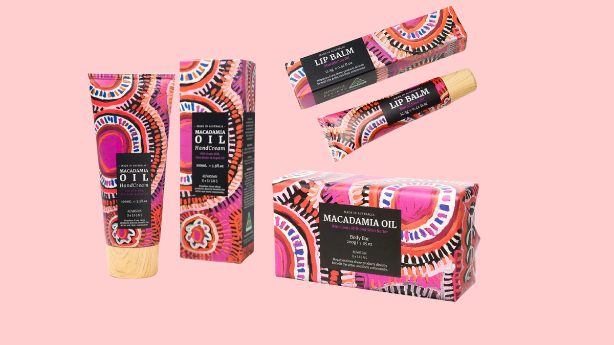 A set of skincare products from Macadamia Oil, including a body oil tube, body oil box, lip balm tube, and lip balm box, all featuring a vibrant pink, orange, and black geometric pattern on a solid pink background.