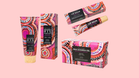 A set of skincare products from Macadamia Oil, including a body oil tube, body oil box, lip balm tube, and lip balm box, all featuring a vibrant pink, orange, and black geometric pattern on a solid pink background.