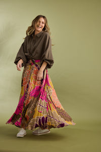 Woman wearing a brown shirt and colorful patterned skirt on a green background