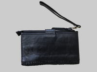 Black leather clutch bag with wrist strap on a light wooden surface