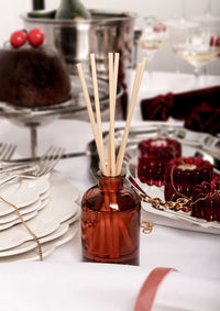 Red diffuser bottle with wooden sticks on a table with desserts and plates.