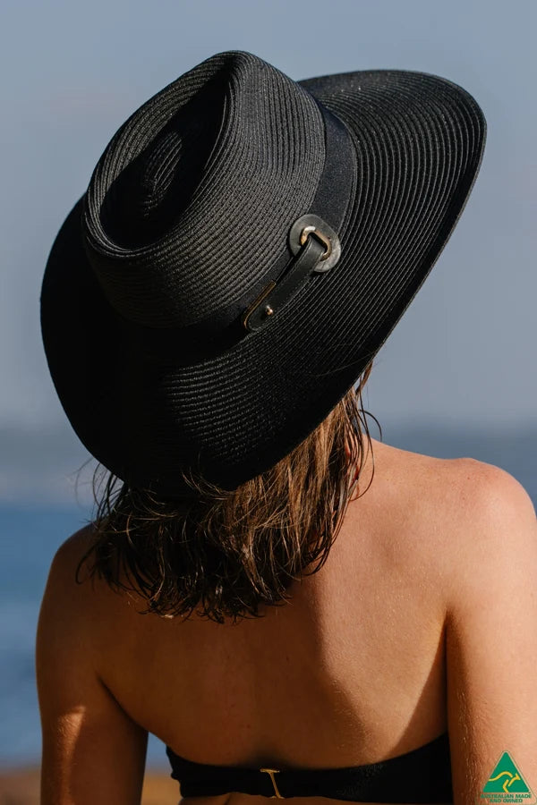 A woman viewed from behind wearing a black woven wide-brim sun hat with a small silver buckle detail.