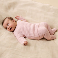 Baby in a pink textured onesie lying on a beige blanket