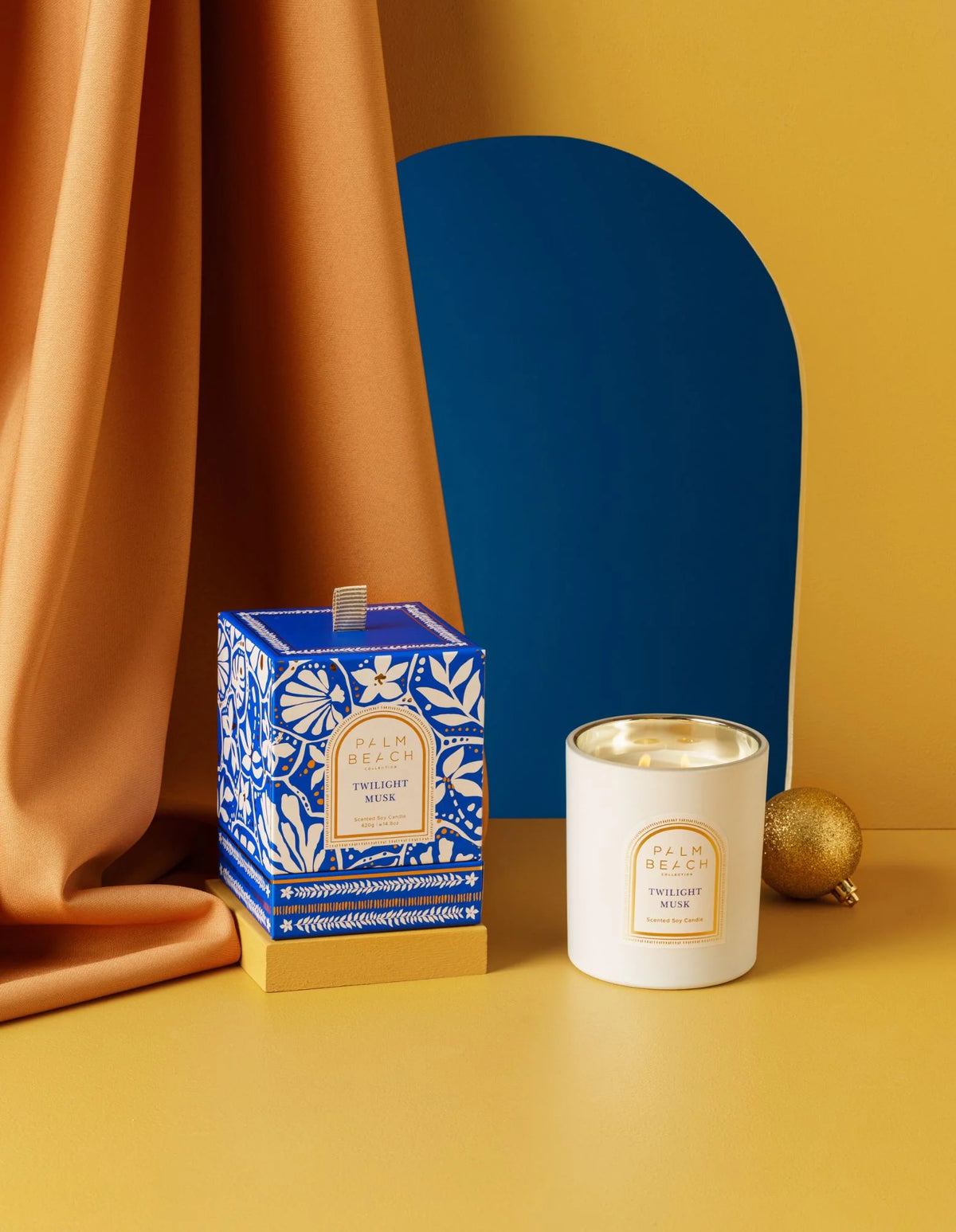 Candle and packaging on a yellow surface with a blue decorative object in the background